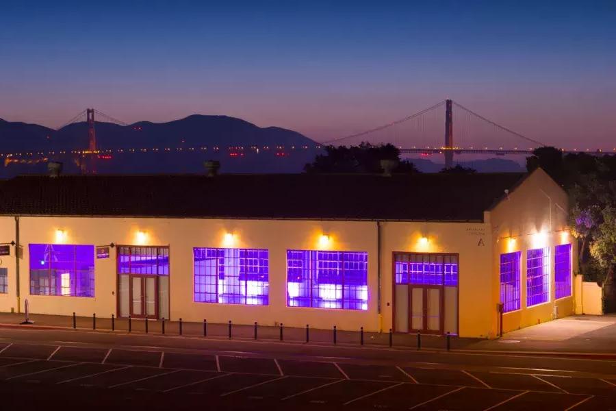 梅森堡大楼在晚上用紫色的室内灯照明, con el puente al fondo.