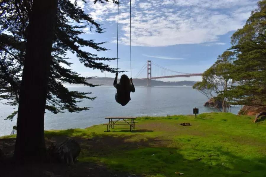 Una mujer se balancea en un columpio de un árbol con vistas al puente Golden Gate. San Francisco, California.