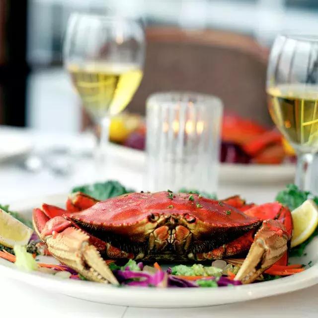 在一家餐厅，一只Dungeness螃蟹坐在盘子里，背景是两杯白葡萄酒.